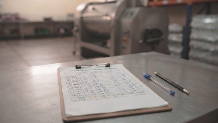 Clipboard with a CCP roaster critical control point record on a steel bench in front of a nut roaster