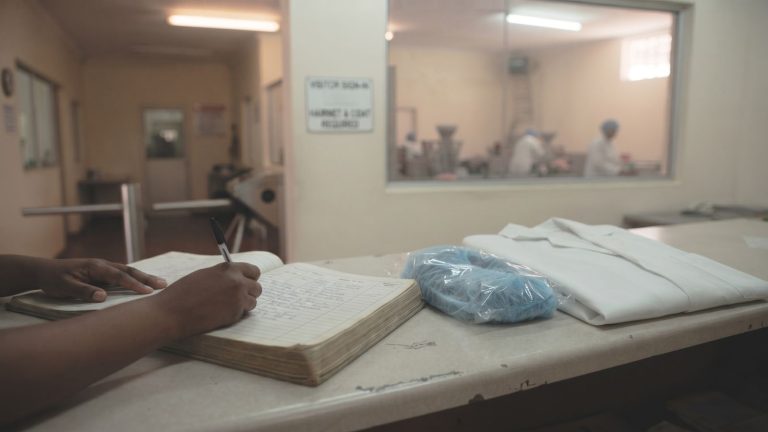 Visitor signing a factory visitors book beside a hairnet and white coat